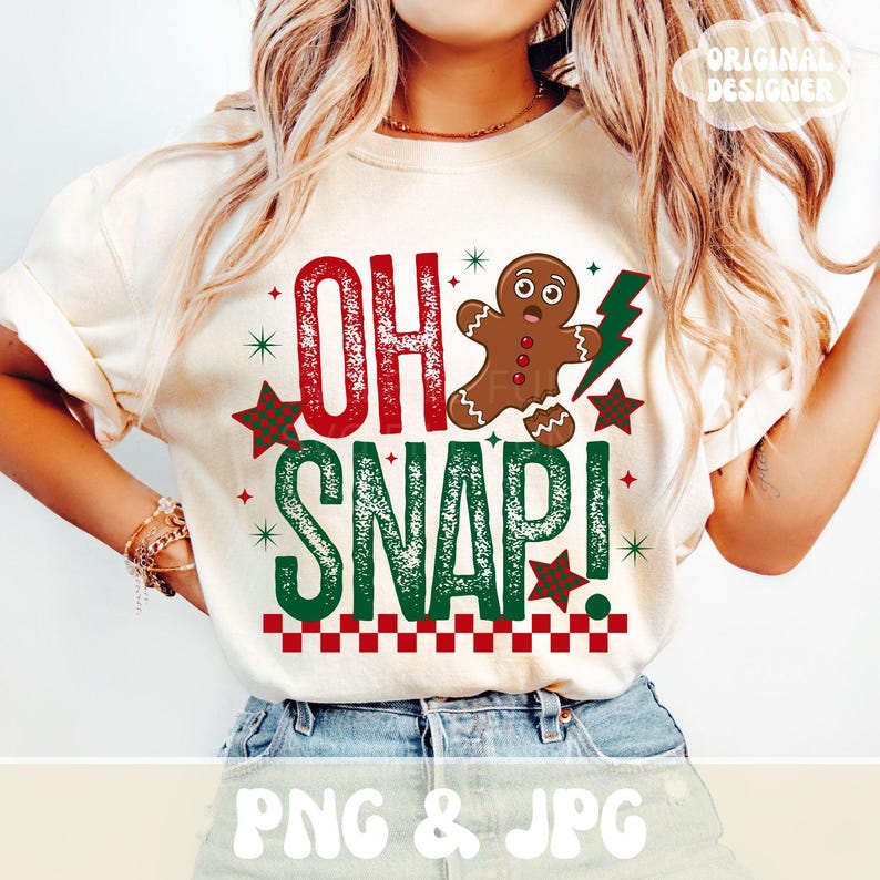 May include: Cream-colored t-shirt with the text "OH SNAP!" in red and green, featuring a gingerbread man and a green lightning bolt. The design includes red and green stars and a checkered border.