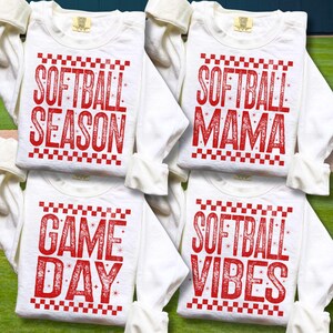 May include: Four white long-sleeved shirts with red text. The shirts have different phrases: "SOFTBALL SEASON", "SOFTBALL MAMA", "GAME DAY", and "SOFTBALL VIBES". Each phrase is in a bold, stylized font with a checkered border.
