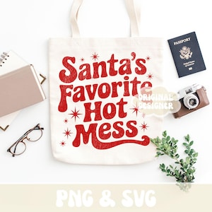 May include: A cream-colored tote bag with the phrase "Santa's Favorite Hot Mess" in red, retro-style lettering. The bag is surrounded by a passport, a vintage camera, glasses, and greenery, suggesting a travel or holiday theme.