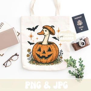 May include: Off-white canvas tote bag featuring a Halloween-themed illustration. The design includes a goose wearing a pumpkin hat, emerging from a carved pumpkin. Black bats and stars surround the pumpkin. The text "PNG & JPG" is at the bottom.