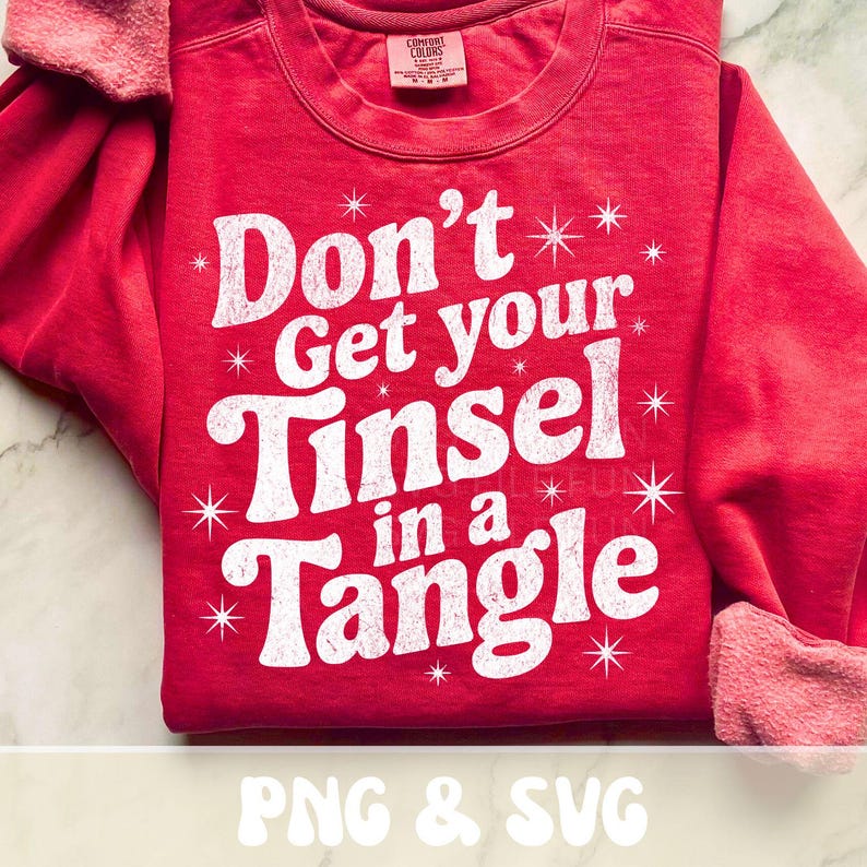 May include: Red sweatshirt with the phrase "Don't Get your Tinsel in a Tangle" in white, with star accents. The sleeves have a pinkish-red cuff. The text "PNG & SVG" is at the bottom.