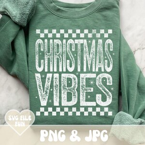 May include: A sage green sweatshirt featuring the words "CHRISTMAS VIBES" in large, distressed white letters, framed by a checkered pattern. The bottom of the sweatshirt has the text "PNG & JPG".