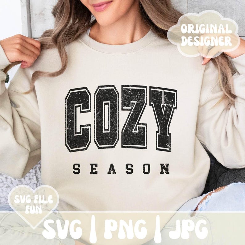 May include: A white sweatshirt with the text "Cozy Season" in black with a distressed, vintage look. The text is in a large, bold font.