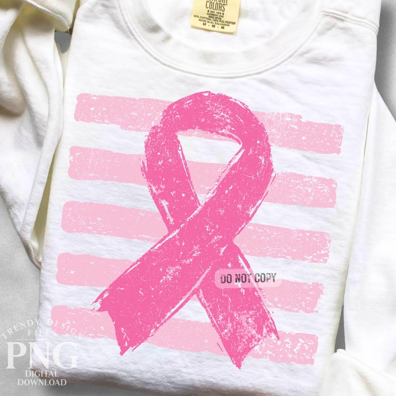 May include: A white long-sleeve sweatshirt featuring a distressed pink awareness ribbon graphic centered over horizontal light pink brushstroke stripes. The garment includes a neck label with text and a watermark reading DO NOT COPY.