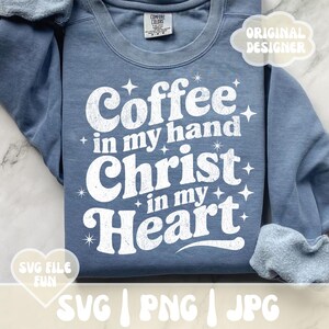 May include: A blue sweatshirt with the text "Coffee in my hand, Christ in my Heart" in white, with star accents. The sweatshirt has a crew neck and long sleeves. The words "Original Designer" and "SVG File Fun" are also visible.