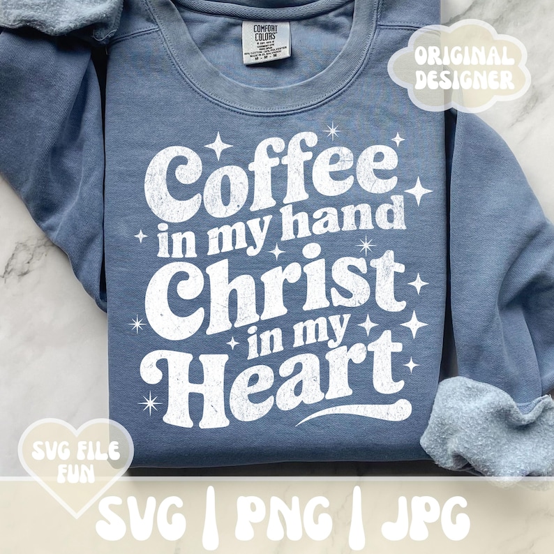 May include: A blue sweatshirt with the text "Coffee in my hand, Christ in my Heart" in white, with star accents. The sweatshirt has a crew neck and long sleeves. The words "Original Designer" and "SVG File Fun" are also visible.