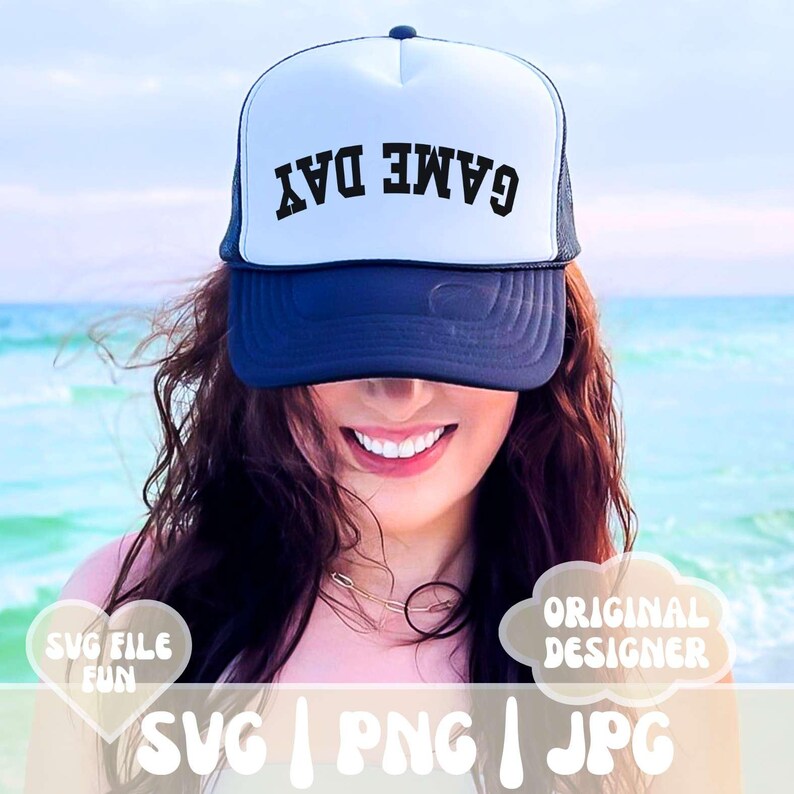 May include: A white and black trucker hat with the text "GAME DAY" in black letters. The hat is worn by a person with long brown hair. The background is a blurry image of a beach.