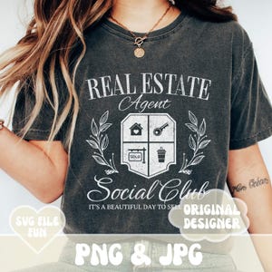 Może przedstawiać: Szary T-shirt z przetartym białym nadrukiem, na kt&oacute;rym widnieje napis "Real Estate Agent Social Club It's a beautiful day to sell". Grafika zawiera dom, klucz, kubek do kawy i znak "Sprzedane".