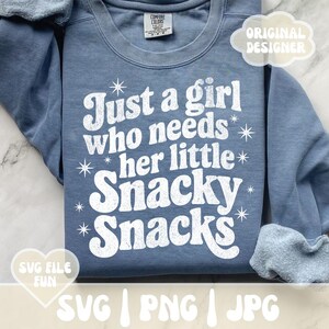 May include: A blue Comfort Colors sweatshirt with the text "Just a girl who needs her little Snacky Snacks" in white. The design includes star accents. The image also shows "Original Designer" and "SVG File Fun" graphics.