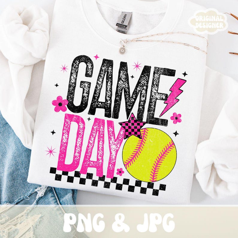 May include: White sweatshirt with the words "GAME DAY" in black and pink, along with a yellow softball graphic. The design includes a pink lightning bolt, stars, and flowers. The sweatshirt has a crew neck.