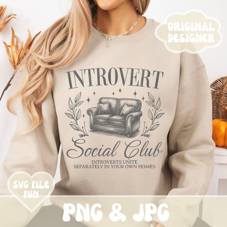 May include: A beige sweatshirt with the text "INTROVERT Social Club" and the words "INTROVERTS UNITE SEPARATELY IN YOUR OWN HOMES" printed on it. The design features a vintage-style illustration of a couch with a floral motif.
