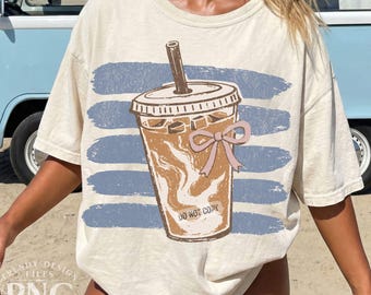 May include: Off-white t-shirt with a coffee graphic, a pink bow, and the text "DO NOT COPY." The design is set against blue horizontal brushstrokes. The shirt is a casual, relaxed fit.