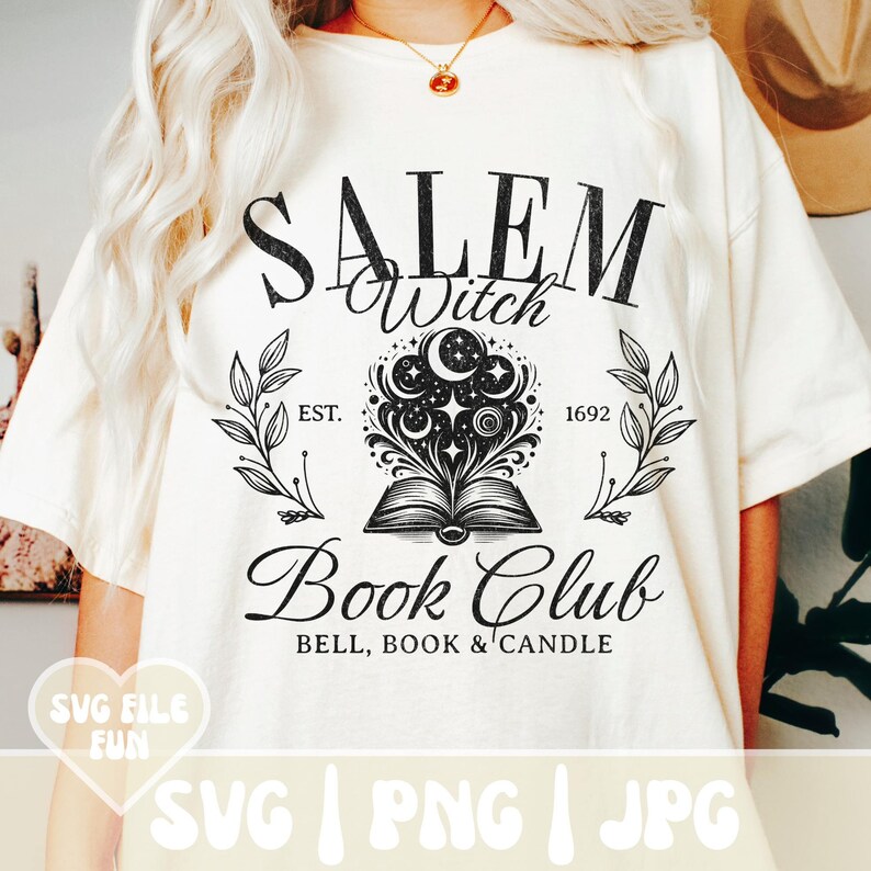 K&ouml;nnte beinhalten: Ein wei&szlig;es T-Shirt mit einem schwarzen grafischen Design, auf dem "Salem Witch Book Club" in einer Vintage-Schrift steht. Die Grafik enth&auml;lt auch ein Buch, aus dem Sterne und Monde herauskommen. Der Text "EST. 1692" ist ebenfalls Teil des Designs.