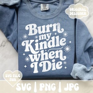 May include: A blue Comfort Colors sweatshirt with the text "Burn my Kindle when I Die" in white, along with star and sparkle graphics. The design includes the words "SVG FILE FUN" and "ORIGINAL DESIGNER".