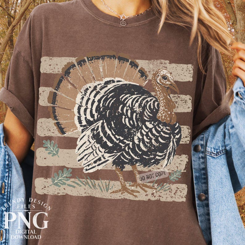 May include: A brown short-sleeve t-shirt featuring a graphic of a turkey with a fanned tail. The design includes horizontal distressed stripes in a light tan color, small leaf accents, and the text DO NOT COPY printed near the turkey's feet.