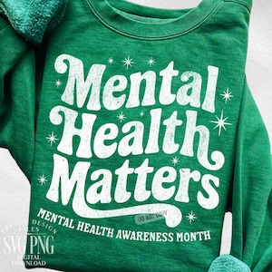 May include: A green sweatshirt with the words "Mental Health Matters" in a distressed white font. The phrase is surrounded by starburst graphics. Below the main text, it reads "Mental Health Awareness Month".