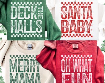 Könnte beinhalten: Vier Sweatshirts mit Rundhalsausschnitt in verschiedenen Farben, jeweils mit einem festlichen Grafikdesign. Die Sweatshirts sind grün, weiß, cremefarben und rot. Die Grafiken zeigen die Slogans "Deck the Halls", "Santa Baby", "Merry Mama" und "Oh What Fun".