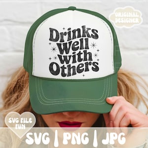 Op de afbeelding: Groene en witte truckerpet met de tekst "Drinks Well With Others" in een zwart, retro lettertype. De pet heeft een gebogen klep en een mesh achterkant. Het ontwerp bevat sterren.
