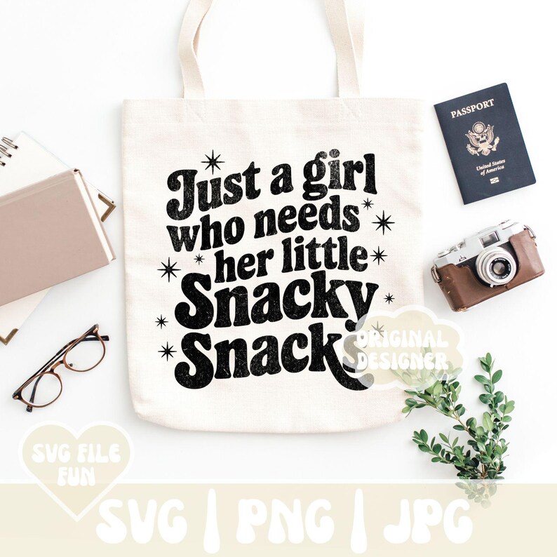 May include: A cream-colored tote bag with the text "Just a girl who needs her little Snacky Snack" in black. The image also includes a passport, a vintage camera, and a pair of glasses.