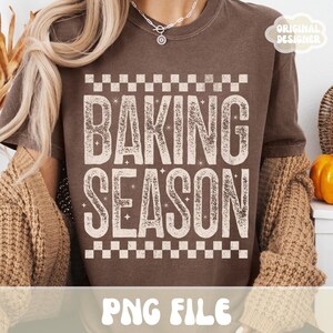 May include: Brown t-shirt with the words "BAKING SEASON" in a distressed, off-white font. The text is framed by a checkered pattern at the top and bottom. The shirt also has the text "PNG FILE" at the bottom.