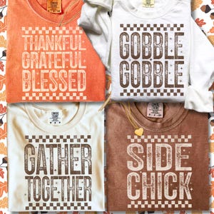 Może przedstawiać: Cztery koszulki Comfort Colors z jesiennym tekstem. Koszulki są pomarańczowe, białe, kremowe i brązowe. Pomarańczowa koszulka m&oacute;wi "THANKFUL GRATEFUL BLESSED". Biała koszulka m&oacute;wi "GOBBLE GOBBLE". Kremowa koszulka m&oacute;wi "GATHER TOGETHER". Brązowa koszulka m&oacute;wi "SIDE CHICK."