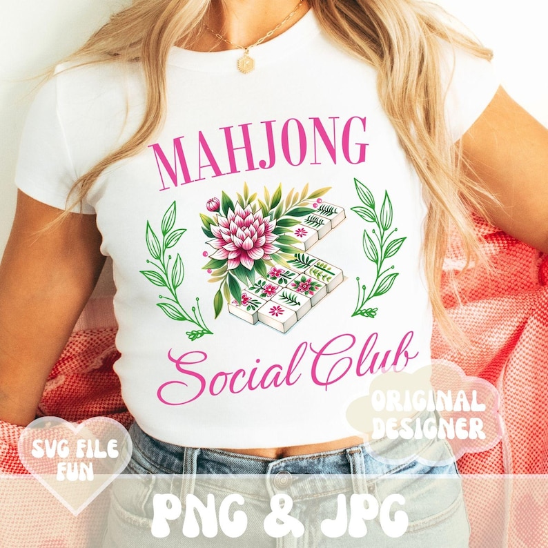 Puede incluir: Camiseta blanca con texto rosa que dice "Mahjong Social Club" y un dise&ntilde;o floral con fichas de mahjong. El dise&ntilde;o incluye una flor rosa, hojas verdes y fichas de mahjong blancas.