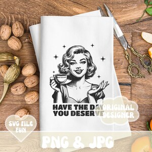 Puede incluir: Pa&ntilde;o de cocina blanco con una ilustraci&oacute;n retro en blanco y negro de una mujer sosteniendo una taza de t&eacute;. El texto "HAVE THE DAY YOU DESERVE" est&aacute; impreso debajo. El pa&ntilde;o est&aacute; sobre una superficie de madera.
