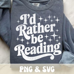 Op de afbeelding: Een donkergrijs sweatshirt met de witte tekst "I'd Rather be Reading" in een retro lettertype. Het ontwerp bevat sterrenburst graphics. Het sweatshirt is van het merk Comfort Colors.