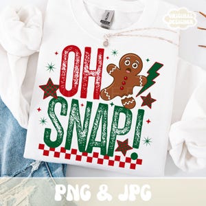 May include: White sweatshirt with the text "OH SNAP!" in red and green, featuring a gingerbread man and star graphics. The design includes a red and white checkered border at the bottom. The words "PNG & JPG" are at the bottom.