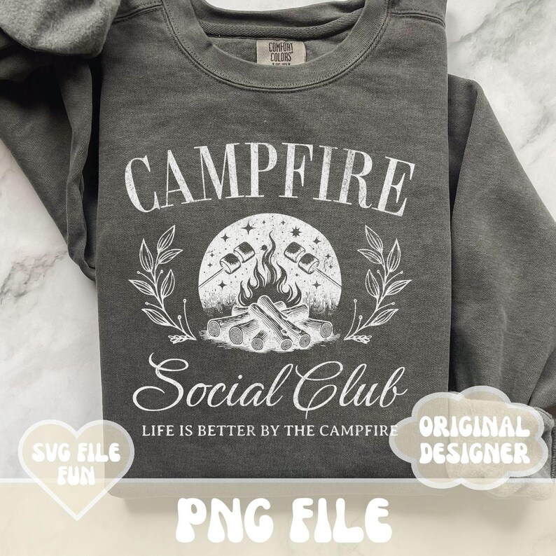Może przedstawiać: Szara bluza z białym nadrukiem przedstawiającym ognisko z piankami i tekstem "Campfire Social Club" oraz "Life is better by the campfire".