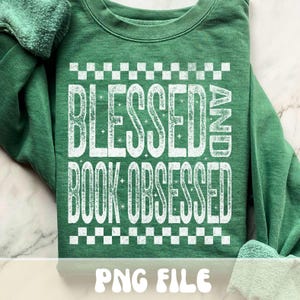 以下が含まれることがあります： 「BLESSED AND BOOK OBSESSED」の白文字がプリントされたグリーンのスウェットシャツ。テキストの上と下には市松模様があり、「PNG FILE」の文字がスウェットシャツの下部にあります。