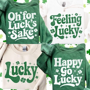 Pode incluir: Quatro camisolas com designs temáticos do Dia de São Patrício. As camisolas são verdes, brancas e bege. Cada camisola tem um design de texto verde diferente, incluindo as frases "Oh for Luck's Sake", "Feeling Lucky", "Lucky" e "Happy Go Lucky".