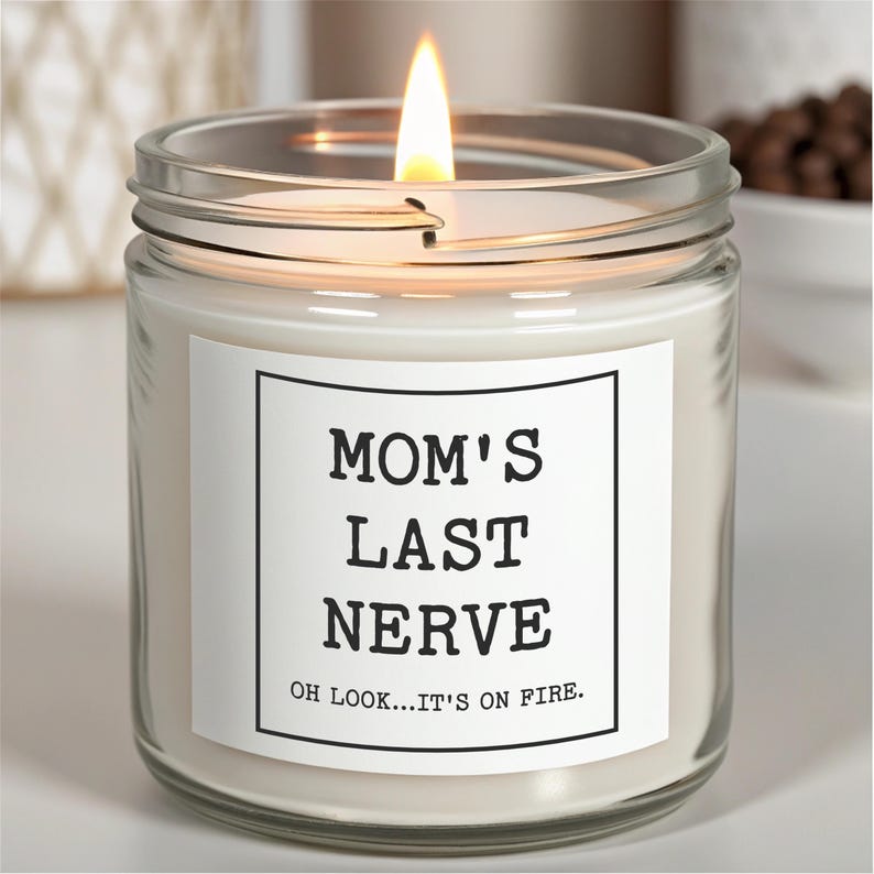May include: A white candle in a clear glass jar with a white label that reads "Mom's Last Nerve Oh Look...It's On Fire."