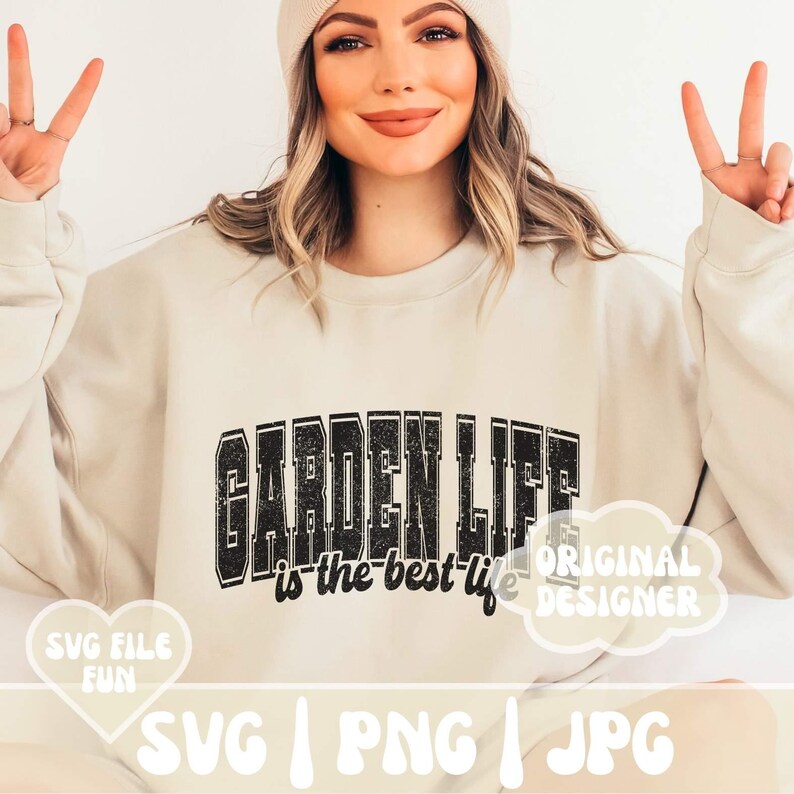 May include: A white sweatshirt with the text "GARDEN LIFE is the best life" in black with a distressed look. The text is in a large, bold font. The sweatshirt is being modeled by a person with long brown hair and a white beanie.