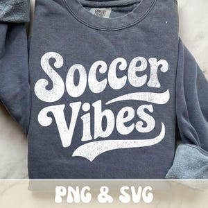 Op de afbeelding: Een donkergrijs sweatshirt met de tekst "Soccer Vibes" in grote, witte letters met een distressed look. De sweatshirt heeft een ronde hals en lange mouwen. De tekst "PNG & SVG" staat onderaan.