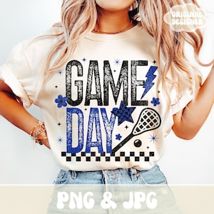 May include: Cream-colored t-shirt with the words "GAME DAY" in black and blue, featuring a lightning bolt, lacrosse stick, and star. The design includes a checkered pattern and floral accents. The words "PNG & JPG" are at the bottom.