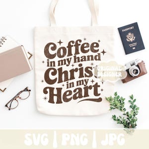 May include: Cream-colored tote bag with the text "Coffee in my hand, Christ in my heart" in brown. The bag is surrounded by a passport, a vintage camera, glasses, a notebook, and greenery. The bottom of the image has the text "SVG | PNG | JPG".