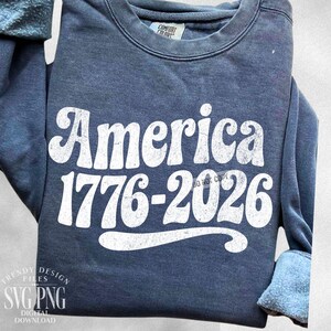 May include: A navy blue sweatshirt with the word "America" in large, white, retro-style font. Below the word "America" is the text "1776-2026" in white. The sweatshirt also has the text "DO NOT COPY" in white. The sweatshirt is from Comfort Colors.