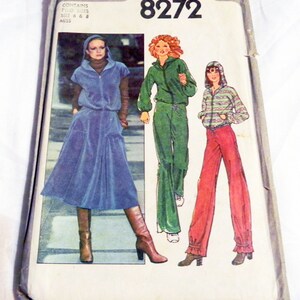 May include: Vintage Simplicity sewing pattern 8272. The pattern envelope features illustrations of three different outfits: a blue hooded dress, a green tracksuit, and red pants with a striped hooded top. The envelope is slightly worn and has the price $2.00 printed on it.