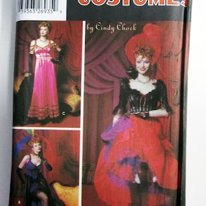 May include: Simplicity Costumes sewing pattern featuring three costume designs. The package displays images of women in elaborate outfits, including a pink gown, a red and purple skirt, and a blue dress. The brand name and designer's name are also visible.
