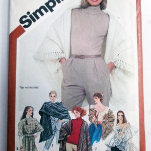 May include: A Simplicity sewing pattern envelope 5210 featuring illustrations of various shawl and cape designs. The main image shows a cream-colored fringed shawl worn over a turtleneck and trousers. Additional illustrations display patterned, solid, and ruffled cape styles with numbered labels.