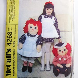 May include: A McCall's 4268 sewing pattern envelope featuring Raggedy Ann and Andy dolls. The package displays a child wearing a matching floral dress and white apron, alongside two fabric dolls with red yarn hair, white aprons, and striped socks.