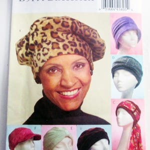 May include: A Butterick B5111 sewing pattern envelope featuring various hat styles. The main image shows a leopard print beret. Smaller images display hats in purple, dark gray, red, light green, black, and a patterned headscarf style.