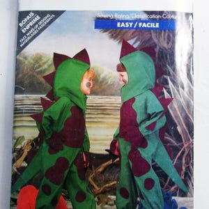 May include: Butterick 5798 sewing pattern envelope featuring a green and maroon dinosaur costume with a hooded jumpsuit, spikes, and tail. The package includes bonus face make-up designs and is labeled with an easy sewing rating.
