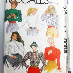 May include: A McCall's 8085 sewing pattern envelope featuring illustrations of six different blouse styles. The designs include various high-neck, long-sleeve tops with ruffles, pleats, and patterns, paired with skirts or pants, labeled with letters A through F.