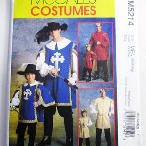 May include: A McCall's Costumes sewing pattern envelope, M5214, featuring illustrations of historical-style outfits. The blue tabard with a white cross, a red tunic with a gold cape, and a beige tunic are shown on adults and children.
