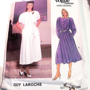 May include: Vintage Vogue Patterns sewing pattern featuring two dress designs. One dress is white with a pleated skirt and a belted waist. The other is a long purple dress with long sleeves and a jeweled belt. The pattern is labeled "Guy Laroche" and "Paris Original".
