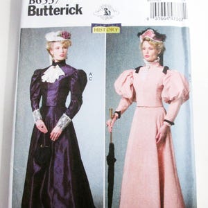 May include: Butterick sewing pattern B6537 featuring two historical-style outfits. One is a dark purple long-sleeved dress with a white lace collar and cuffs. The other is a light pink long-sleeved dress with puffed sleeves and black trim.