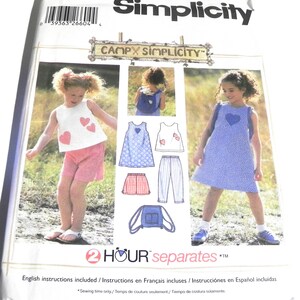 May include: A Simplicity 5617 sewing pattern envelope for children's clothing, labeled size AA 2,3,4. The package features illustrations and photographs of a sleeveless top with heart appliqués, a dress, shorts, pants, and a small backpack.