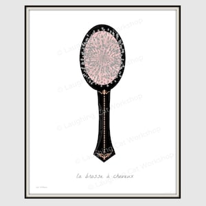 May include: A black and white hairbrush with a pink and gray bristle head. The handle is decorated with gold accents and the text "la brosse à cheveux" is printed below the brush.
